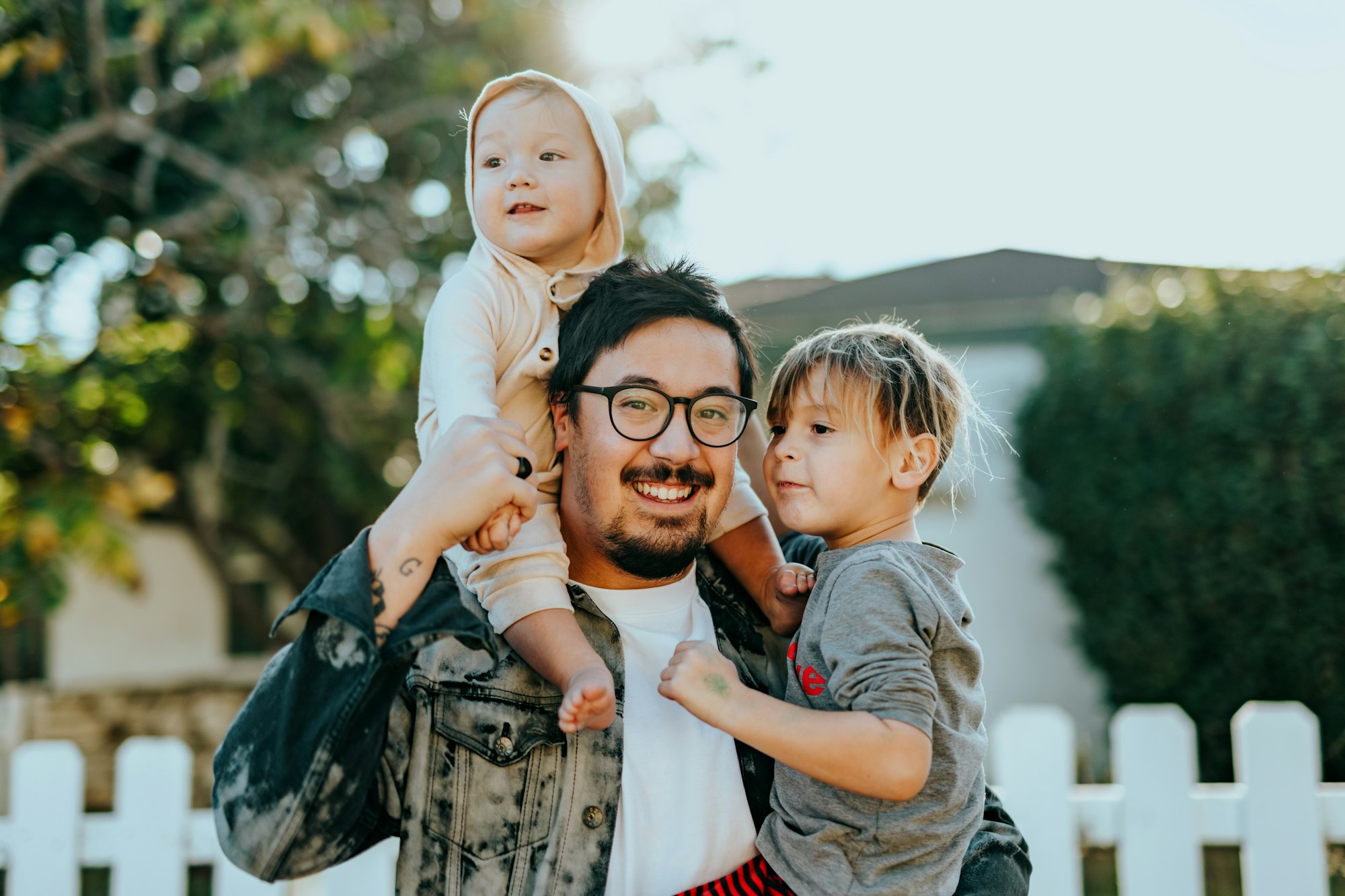 A father holding his two children in front of their home